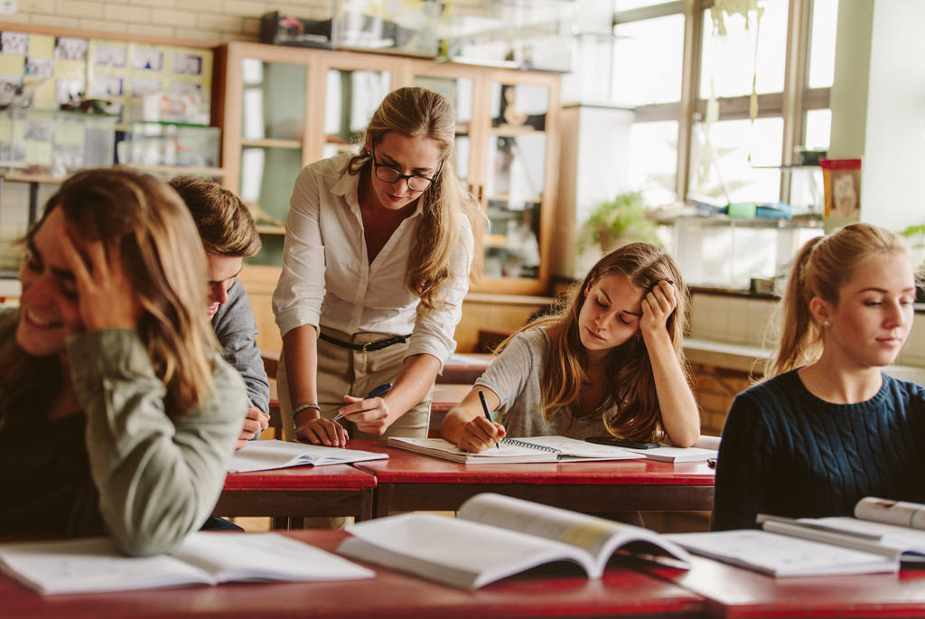 Eine promovierte wissenschaftliche Mitarbeiterin befindet sich in einem Seminarraum inmitten ihrer Studierenden. Sie gibt gerne Lehre, ist sich jedoch auch bewusst, dass sie ihr wissenschaftliches Profil noch durch andere Leistungen schärfen muss.