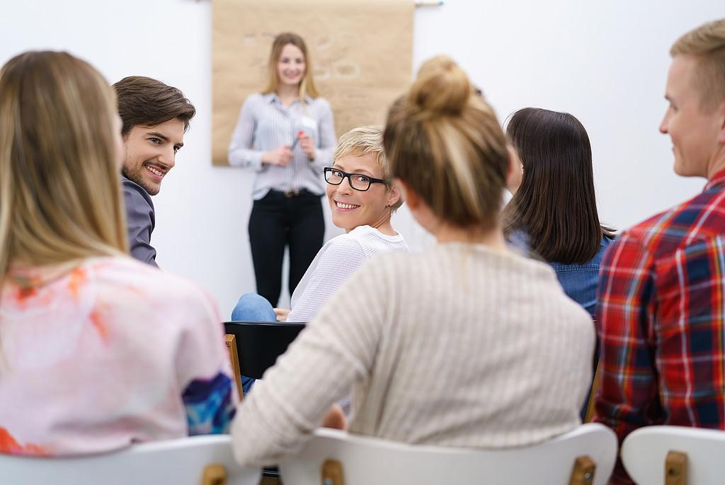 Eine junge Doktorandin stellt in ihrem Forschungsseminar ihre Ergebnisse vor. Die Gruppe der Seminarteilnehmerinnen und -teilnehmer diskutieren angeregt untereinander.